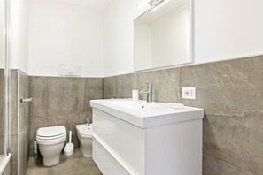 Een moderne badkamer met een wit wastafelmeubel, een toilet en een douchetoilet.