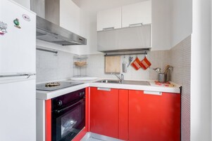 Una cucina con mobili bianchi, un piano di lavoro rosso e elettrodomestici in acciaio inossidabile.