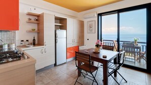 A modern kitchen with white cabinets, a red countertop, and a dining area with a table and chairs. - Taormina Panoramic Seaview Apartment (Taormina)
