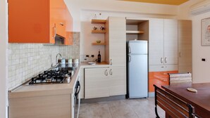 A kitchen with a gas stove, sink, and a refrigerator. There are cabinets and a dining table with chairs. - Taormina Panoramic Seaview Apartment (Taormina)