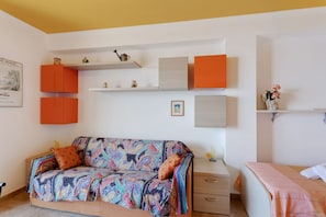 Ein Zimmer mit einer Couch, einem Bett, einem Nachttisch und eingebauten Regalen mit verschiedenen Gegenständen.