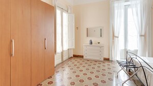 Una camera da letto con un'armadio in legno, una cassettiera bianca, un letto con struttura in metallo e un pavimento decorato.