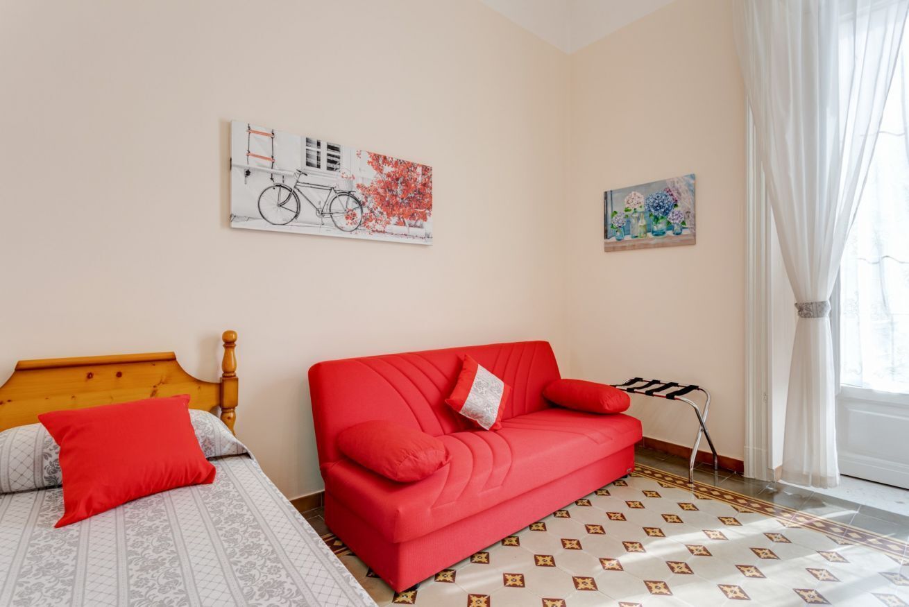 Una habitación con una cama, un sofá rojo y dos cuadros en la pared.