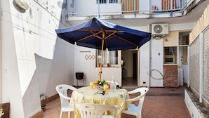 Een terras met een tafel gedekt voor twee personen, een blauwe parasol en witte stoelen.
