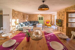 A dining area with a wooden table set for a meal, a stone wall, a green door, and a yellow armchair.