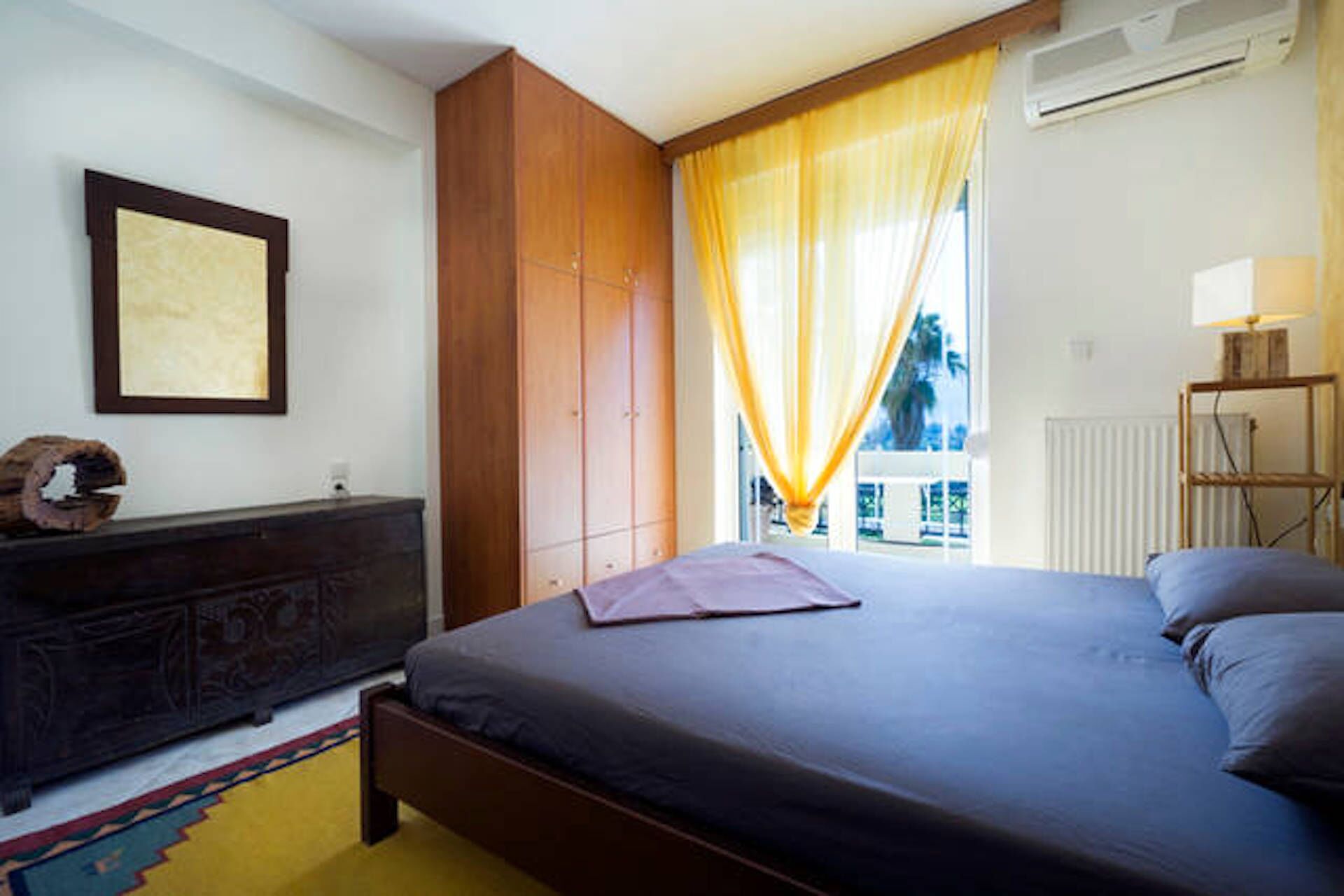 A bedroom with a bed, a dresser, a window with curtains, and an air conditioning unit.