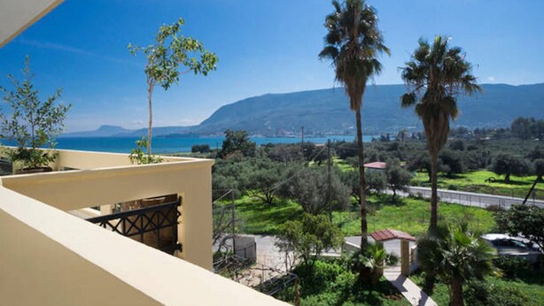 Un balcón con vistas a un paisaje costero, incluyendo palmeras y una cadena montañosa distante.