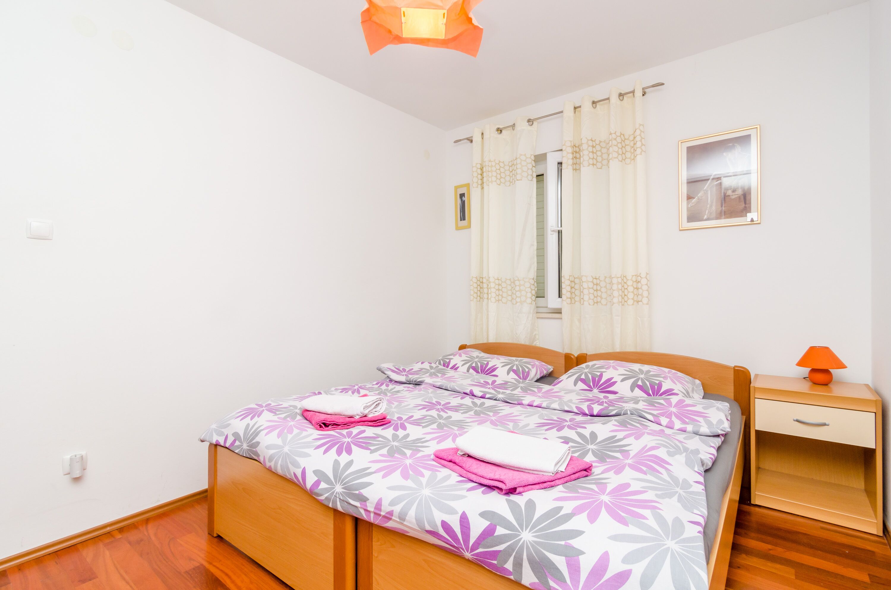 A bedroom with a wooden bed, a nightstand, a lamp, and a window with curtains.