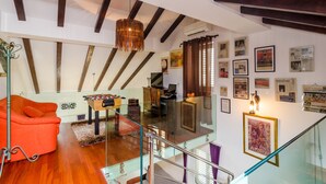 Um amplo loft com vigas de madeira aparentes, escada de vidro, sofá laranja aconchegante e mesa de bilhar.