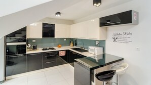 Uma cozinha moderna com armários preto e branco, uma ilha de vidro e um micro-ondas. Há um aviso fixado na parede com regras da cozinha.
