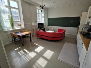 A modern classroom with a blackboard, a red sofa, a dining table with chairs, and a TV.