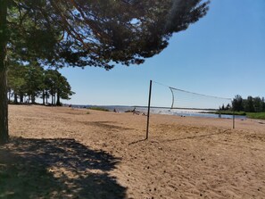 A beach volleyball court with a net, surrounded by trees and a clear sky.