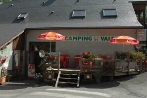 Un edificio con un letrero que dice "CAMPING du VAUDE" y asientos exteriores con sombrillas.