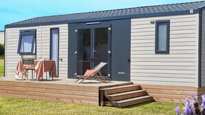 Een stacaravan met terras, een tafel met stoelen en een ligstoel.