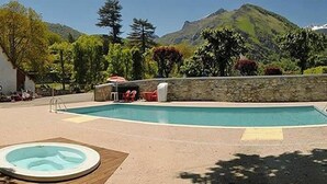 Zwembad met een jacuzzi, omringd door een stenen muur en bomen, met bergen op de achtergrond.