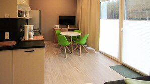 Eine moderne Küche mit Kaffeemaschine, Flachbildfernseher und Essbereich mit grünen Stühlen und einem weißen Tisch.