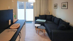 Ein modernes Wohnzimmer mit einem dunklen Sofa, zwei kleinen runden Tischen, einer Holzschneidebrett und einem großen Fenster mit Vorhängen.