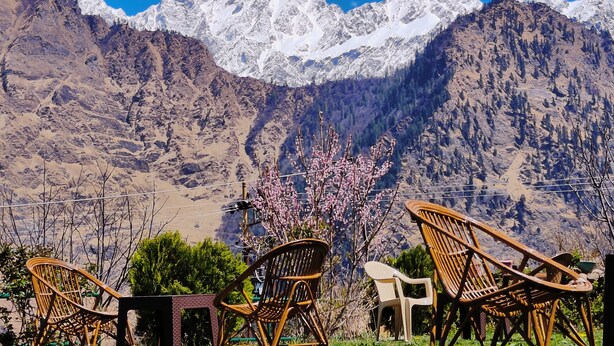 A mountainous landscape with snow-capped peaks and a row of wicker chairs facing the view. - Himalayan High, Auli, By Himalayan Eco Lodges (Joshimath)