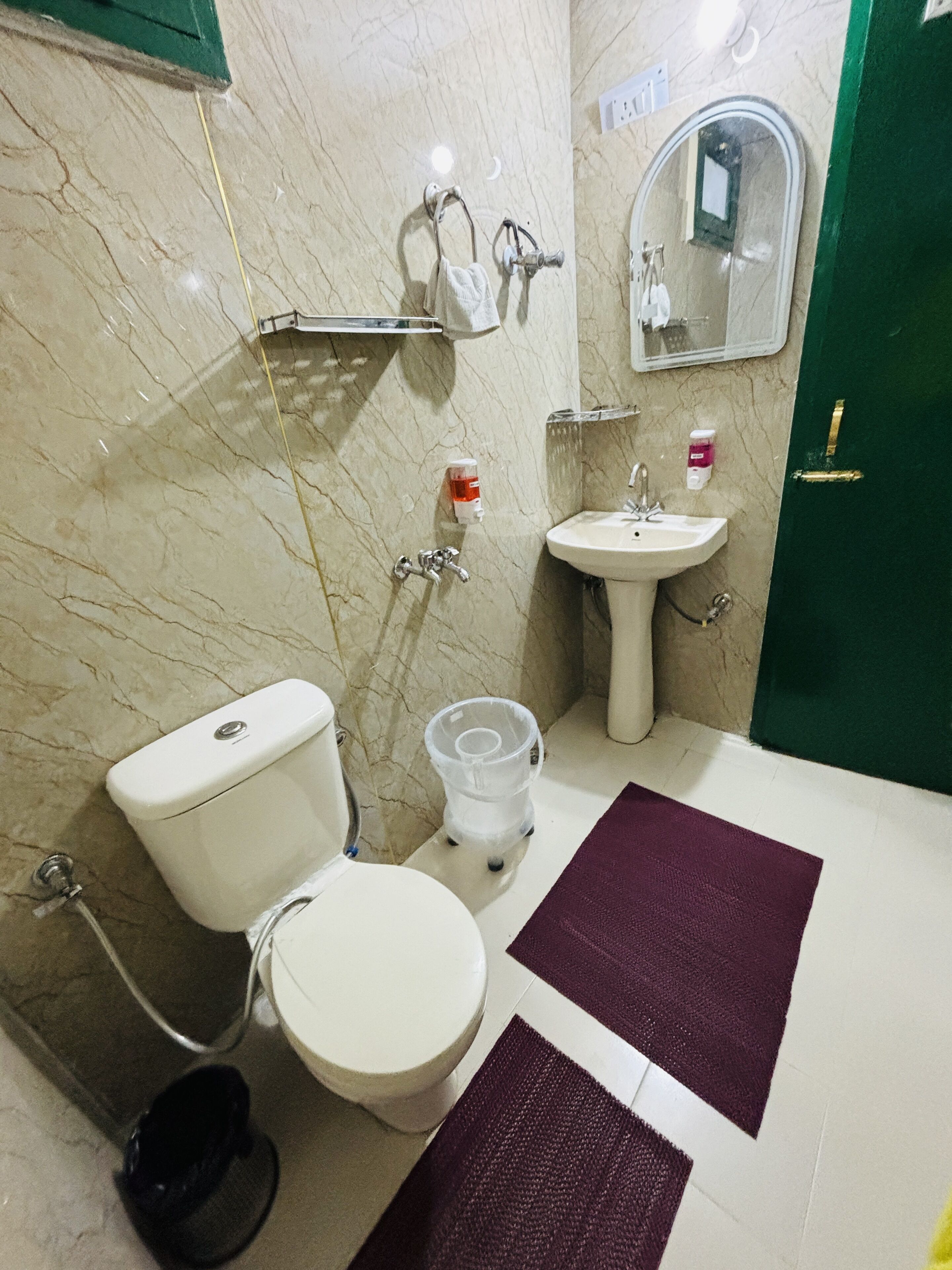 Un baño con inodoro, lavamanos, espejo y una puerta verde.