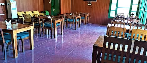 Un comedor con mesas y sillas de madera, una puerta verde y un aire acondicionado instalado.