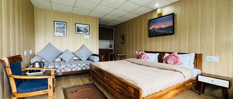 A room with a large bed, a smaller sofa, a wooden chair, and a desk. There are two framed pictures on the wall, a rug on the floor, and a wooden cabinet.