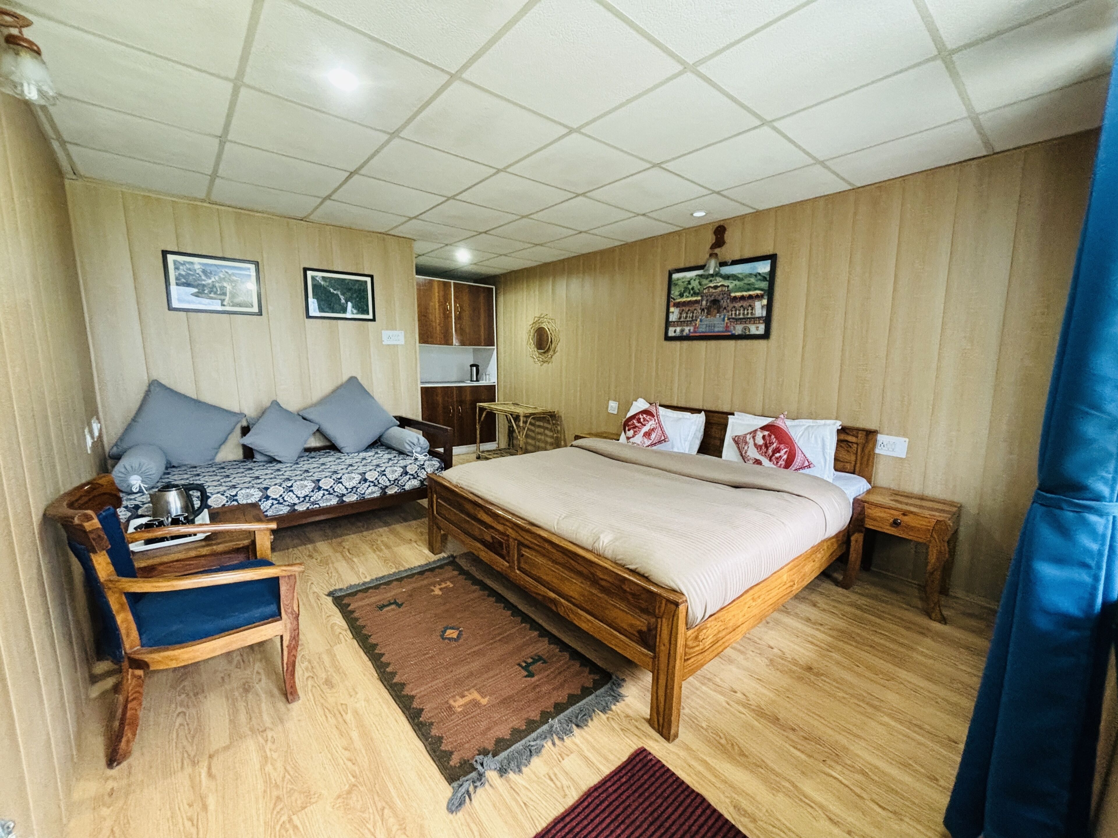A room with a bed, a sofa, a small table, and a chair. There are pictures on the walls and a rug on the floor.