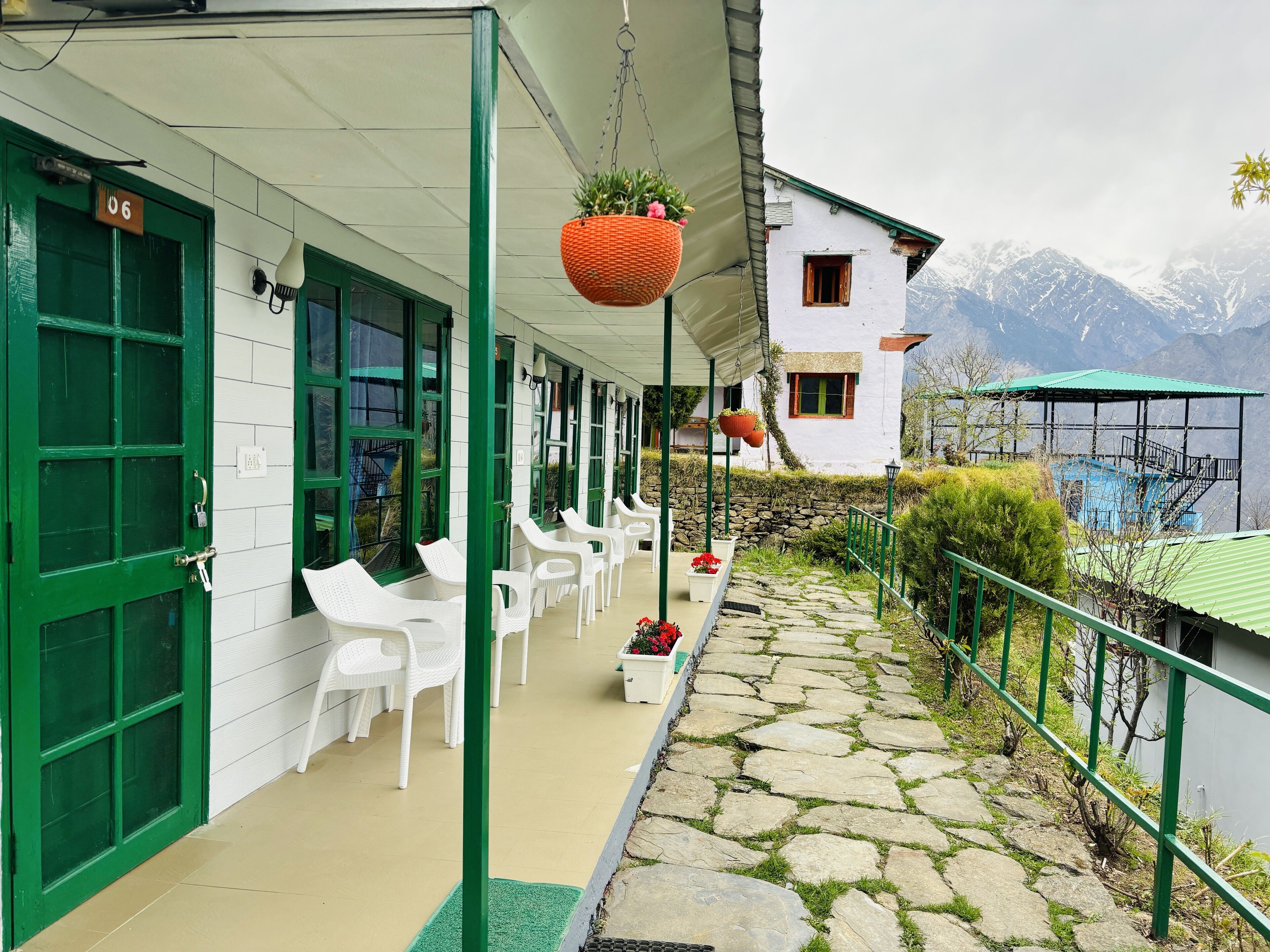A hotel with green doors and windows, outdoor seating, and a stone pathway leading to a mountain view.