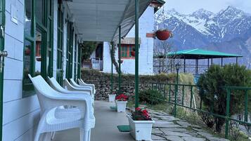 A building with a covered porch, white wicker chairs, a stone wall, and a view of snow-capped mountains.