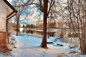 A snow-covered landscape with a lake, trees, and a building with a sloped roof. - Romantic Spa Villa With Fireplace by the Lake (Stjärnsund)