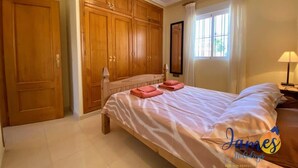A bedroom with a large bed, wooden wardrobe, and a window with curtains.