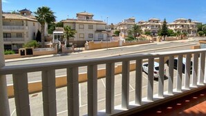 A balcony with a view of a street lined with buildings, a clear sky, and a parking area.