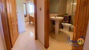A hallway leading to a bathroom with a sink, bidet, and mirror.