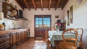 Une cuisine avec des meubles en bois, un pare-feu en carrelage, une table à manger avec des chaises et une vue à travers une porte.