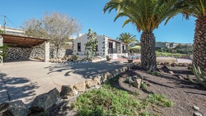 Un bâtiment doté d’une façade en pierre, d’un patio couvert et de palmiers.