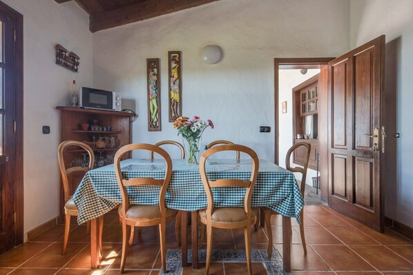 Un coin repas avec une nappe à carreaux, des chaises en bois, un vase de fleurs et un mur orné d’œuvres d’art.