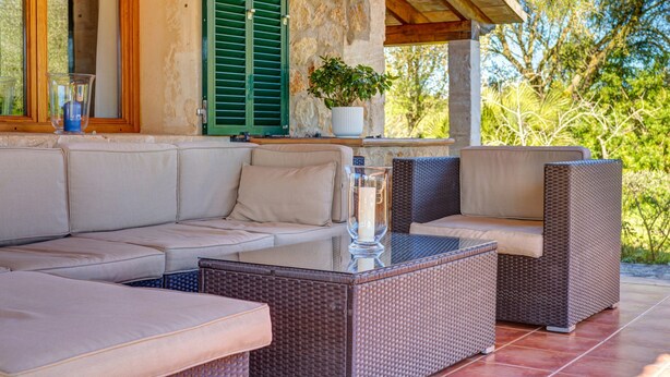 An outdoor seating area with a sofa, wicker tables, and a potted plant. - Country House “Can Vaja”, a Mallorquin style property with Pool, Terrace & Garden (POLLENSA)