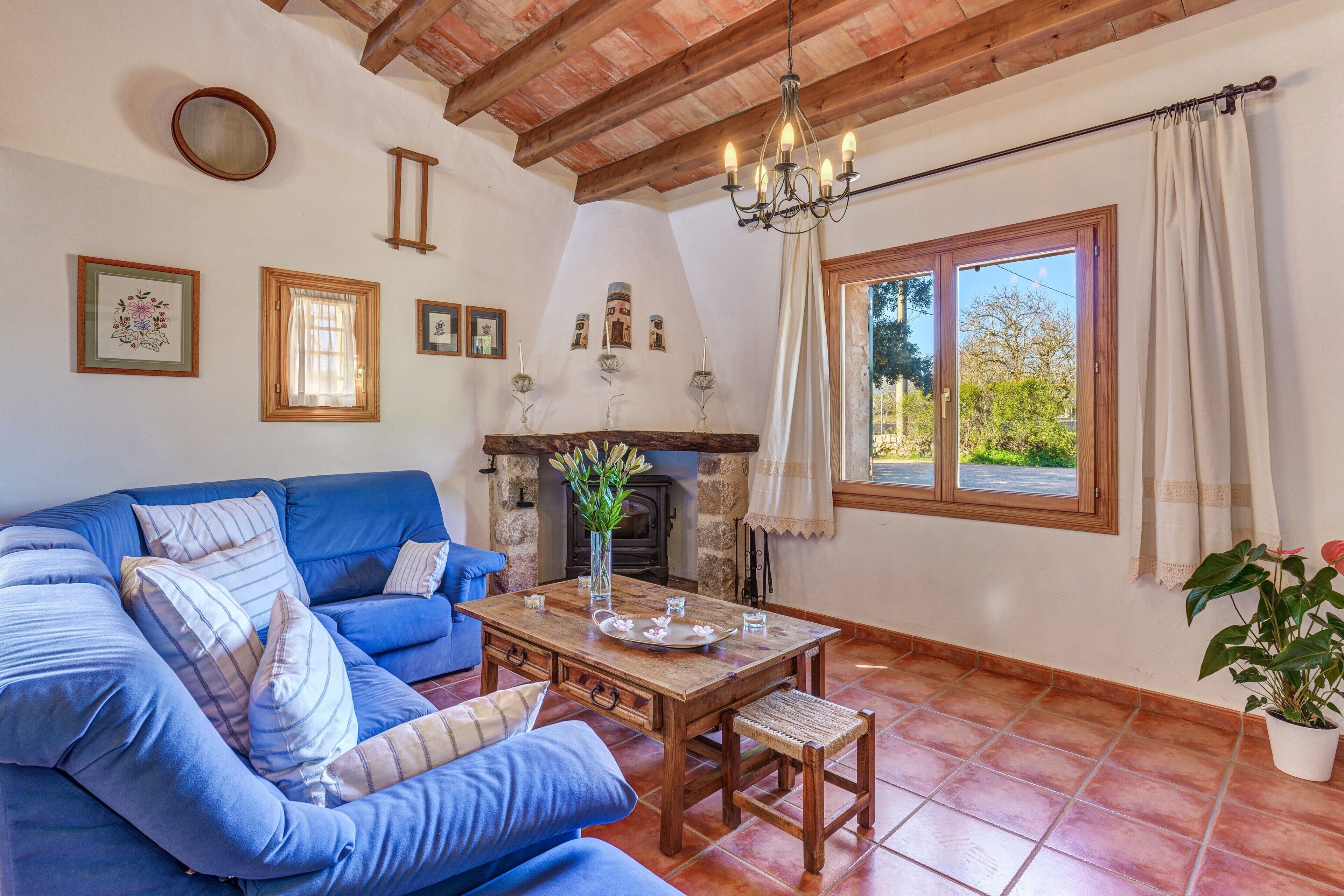 A cozy living room with a blue sofa, a wooden table, a fireplace, and a large window with curtains.