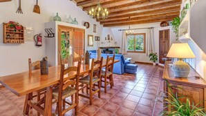 A rustic kitchen with wooden beams, a dining table with chairs, a blue sofa, and a chandelier. - Country House “Can Vaja”, a Mallorquin style property with Pool, Terrace & Garden (POLLENSA)