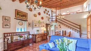A spacious living area with a blue sofa, wooden coffee table, and a staircase leading to an upper level. - Country House “Can Vaja”, a Mallorquin style property with Pool, Terrace & Garden (POLLENSA)
