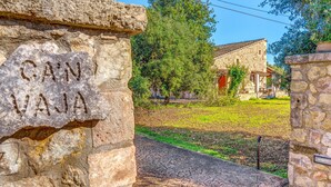 A stone entrance with 'CAÑ VAJA' carved on it, leading to a building with a tiled roof and a grassy area. - Country House “Can Vaja”, a Mallorquin style property with Pool, Terrace & Garden (POLLENSA)
