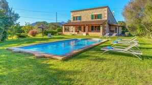 A two-story stone house with a swimming pool, outdoor seating, and a mountain backdrop. - Country House “Can Vaja”, a Mallorquin style property with Pool, Terrace & Garden (POLLENSA)