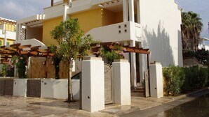 A modern two-story building with a white facade, a wooden pergola, and a small garden area with flowering plants. - Ammiraglia Residence just 200 meters from the beaches - Villa A (Baia Verde)