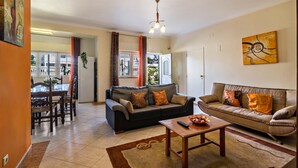 A living room with a sofa, a coffee table, and a dining area with chairs and a table. - Apartment "Anastácio" with Garden View, Shared Pool, Wi-Fi & Balcony (Olhos de Água)