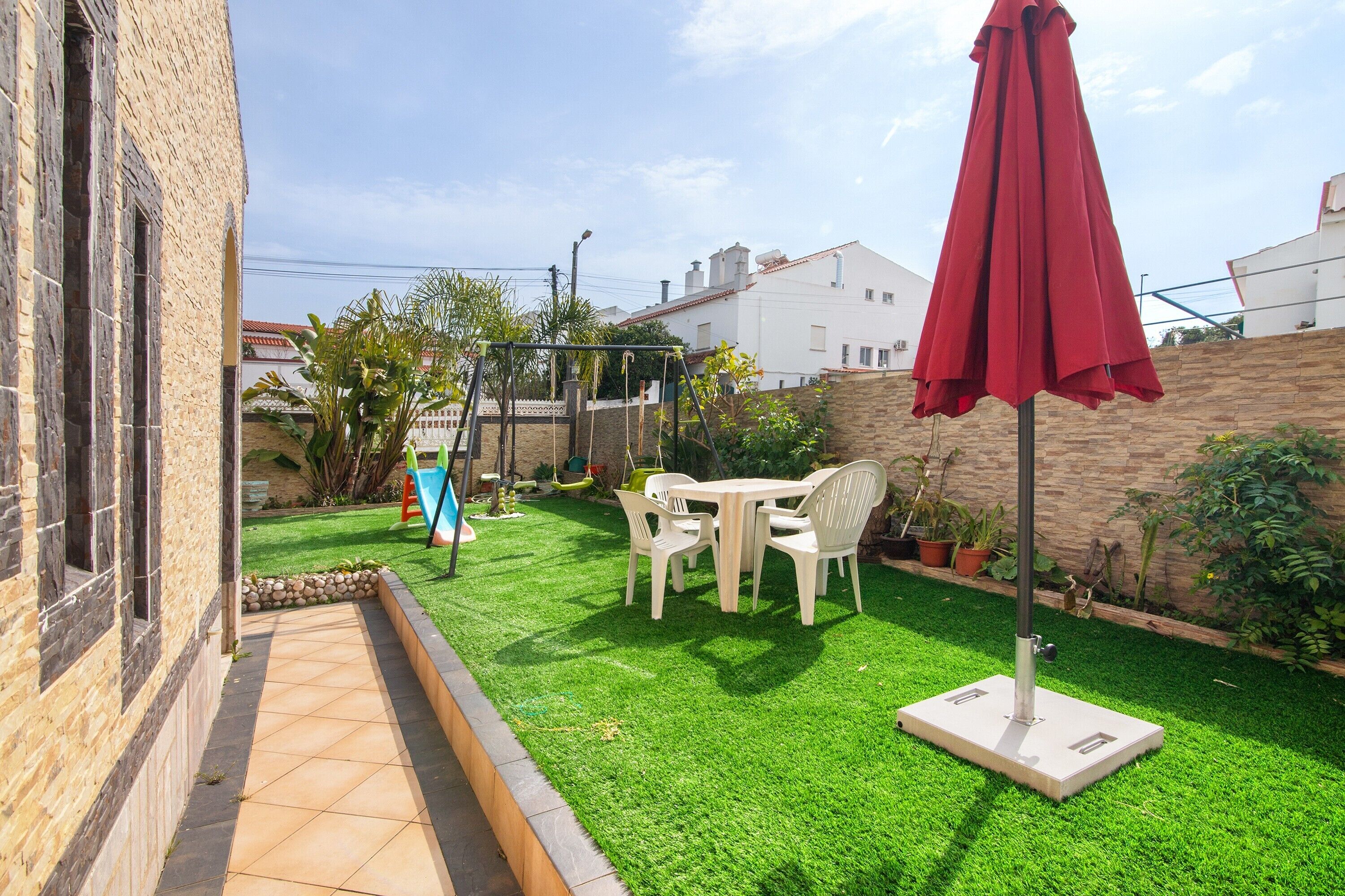 A patio with a table and chairs, a red umbrella, and a small garden area.