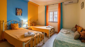 A hotel room with two beds, a window with curtains, an air conditioning unit, and a painting on the wall. - Apartment "Anastácio" with Garden View, Shared Pool, Wi-Fi & Balcony (Olhos de Água)