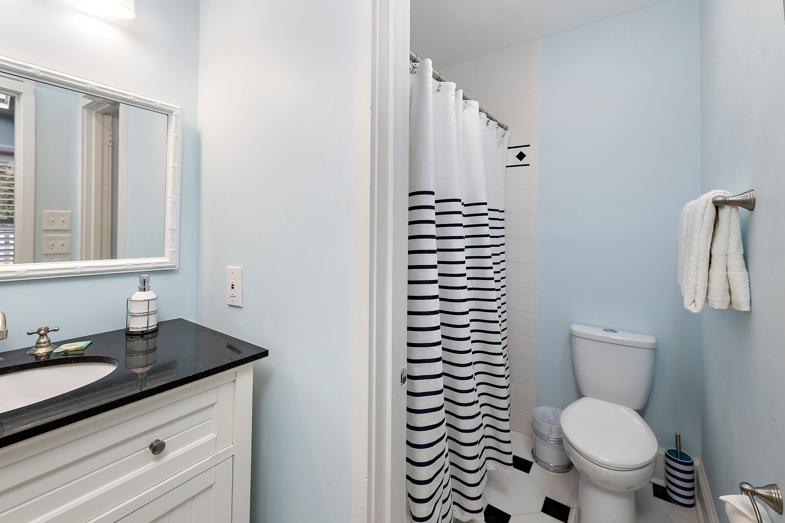 A bathroom with a white sink, a mirror, a striped shower curtain, a toilet, and a towel rack.