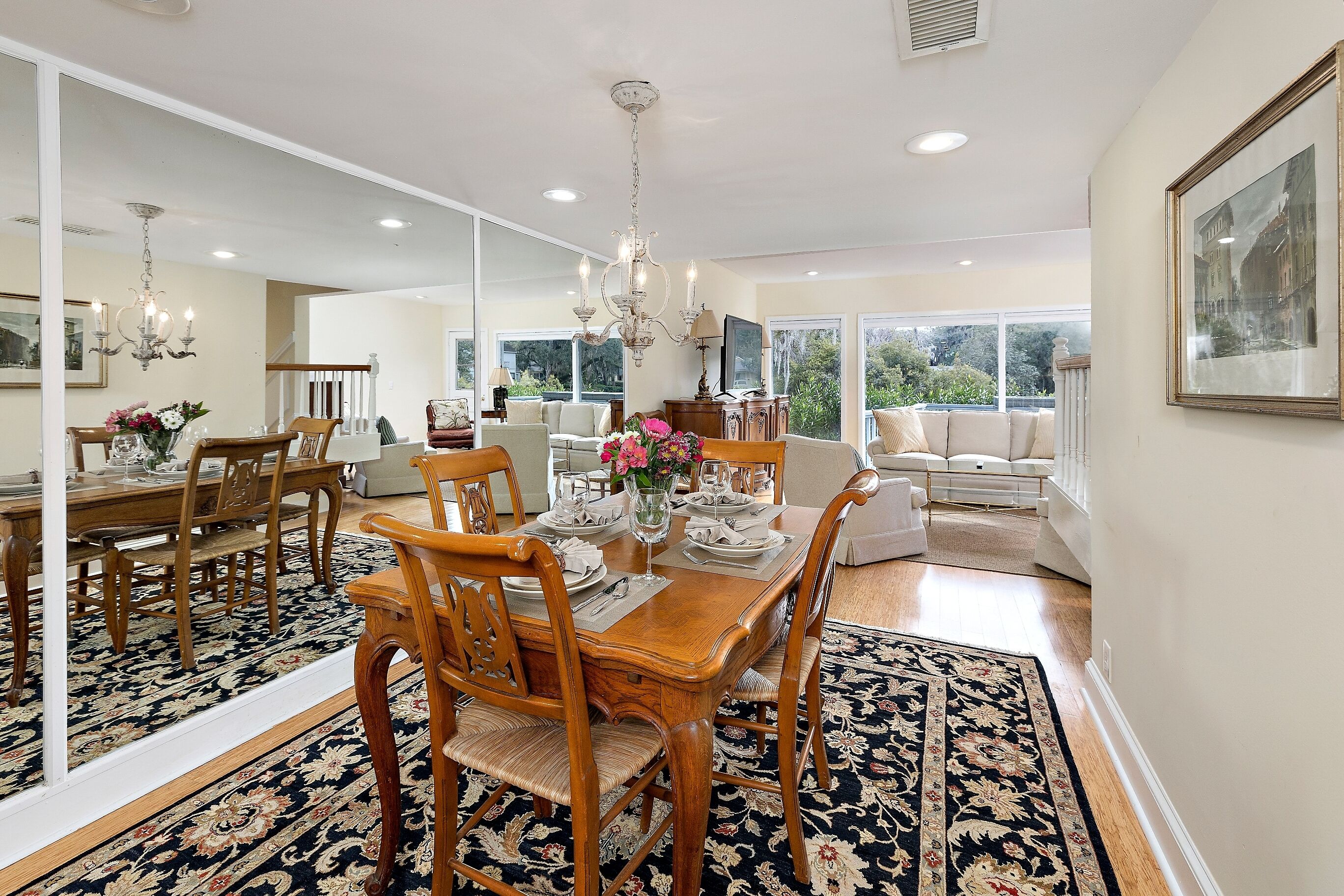 A dining area with a wooden table set for four, surrounded by chairs, a chandelier, and a large mirror.