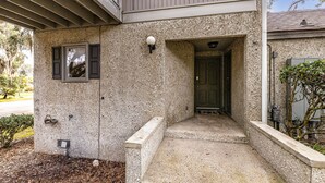 Una casa con fachada de concreto, una puerta principal y un ventanal pequeño con contraventanas.