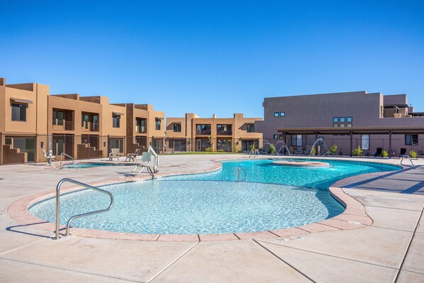Una piscina de diseño curvo, rodeada por una terraza de concreto y un edificio con techo plano y múltiples ventanas.