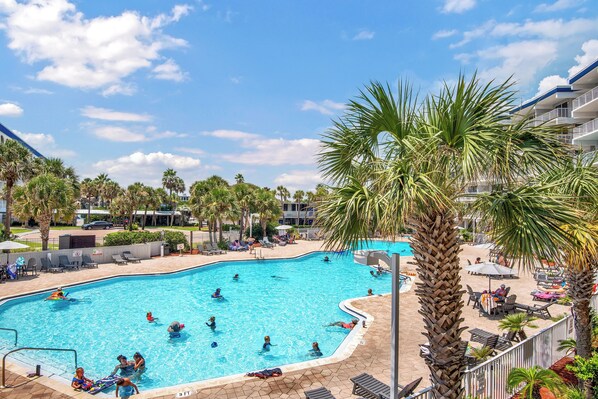 Une piscine entourée de palmiers et de chaises longues, sous un ciel bleu azur.